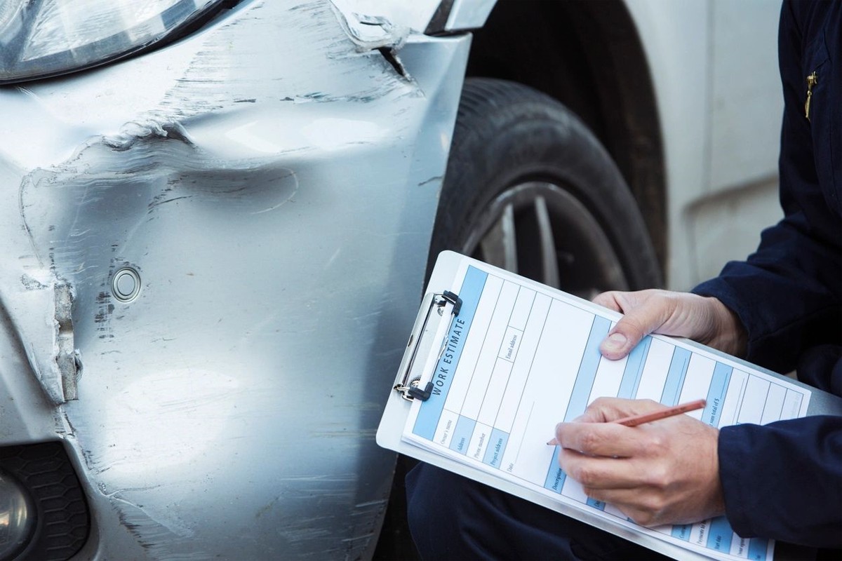 A person filling out a form in front of a damaged car